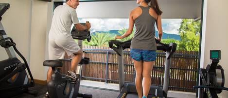 A gym with treadmills, stationary bikes, and a TV on the wall.