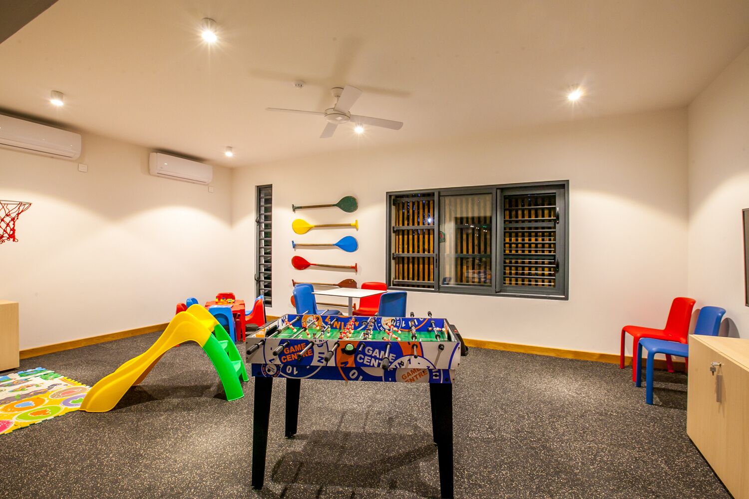 Una sala de juegos para niños con mesa de fútbol de mesa, un tobogán y diversos juguetes.