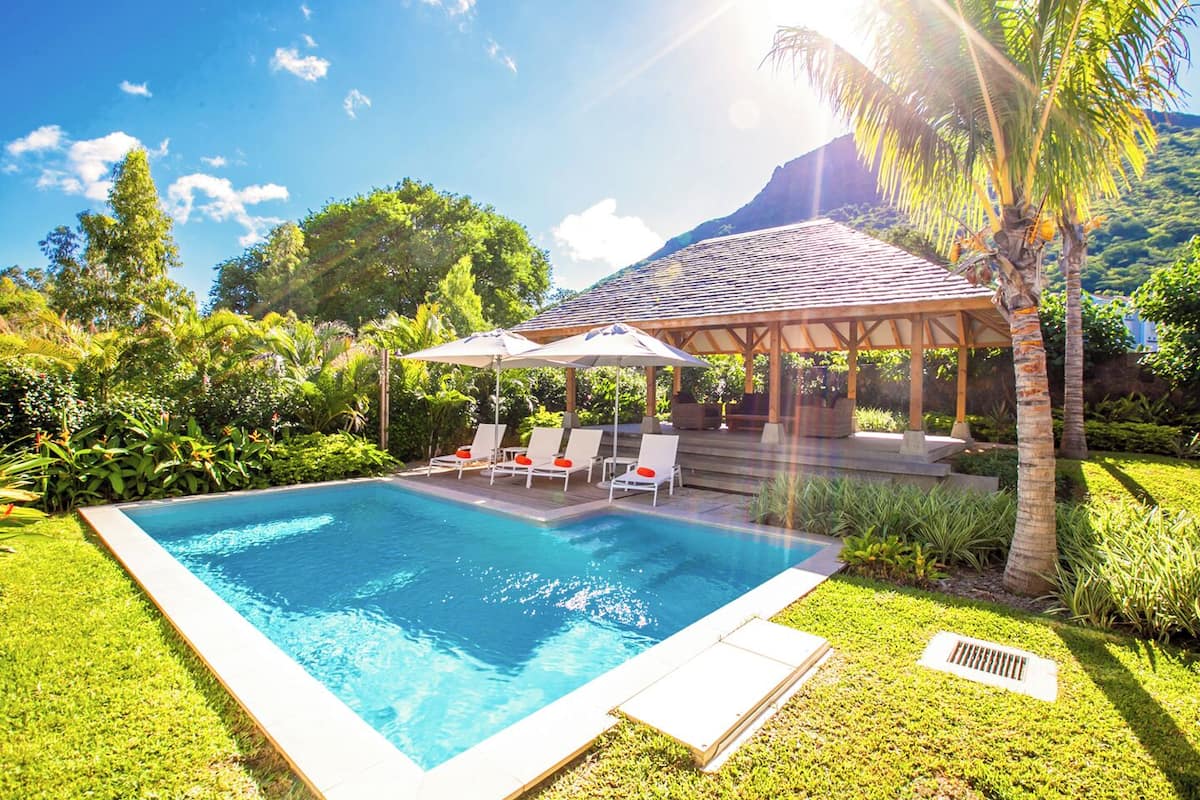 Una piscina rectangular con sillas de descanso y un pabellón cubierto.