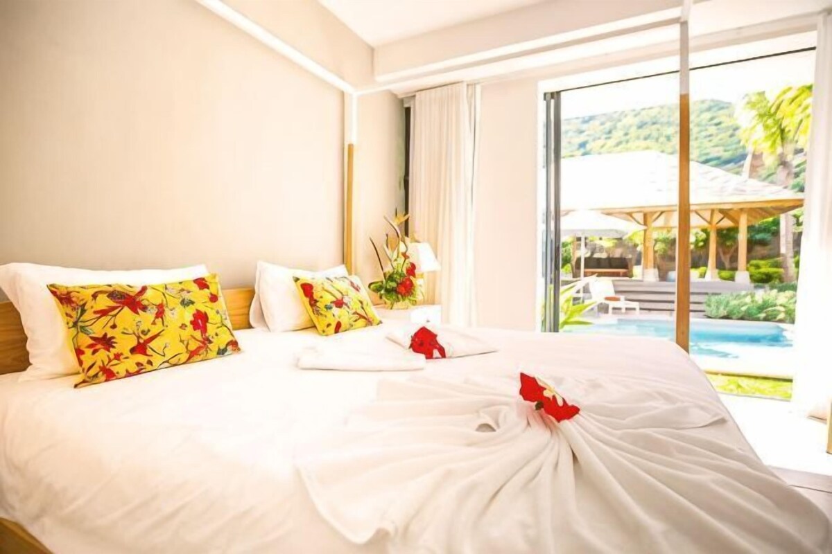 Une chambre d’hôtel avec un grand lit, une vue sur la piscine et un paysage tropical.