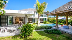 Una casa moderna con piscina, mobiliario exterior y un porche cubierto.