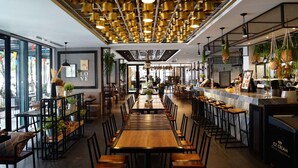 L’intérieur d’un restaurant moderne, avec une longue table en bois, des chaises noires et des plantes suspendues.