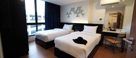 Habitación de hotel con dos camas, un escritorio y una silla. Tiene una ventana con cortinas, un aire acondicionado y un espejo.