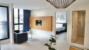 Une chambre d’hôtel moderne dotée d’une grande fenêtre, d’un téléviseur à écran plat fixé au mur, d’une table de chevet, d’une chaise et d’une plante en pot.