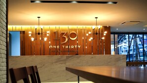Un espace d’accueil avec un mur en bois où figure l’inscription « 30 ONE THIRTY HOTEL & RESORT ». On y trouve deux lampes suspendues et un comptoir d’accueil en marbre.