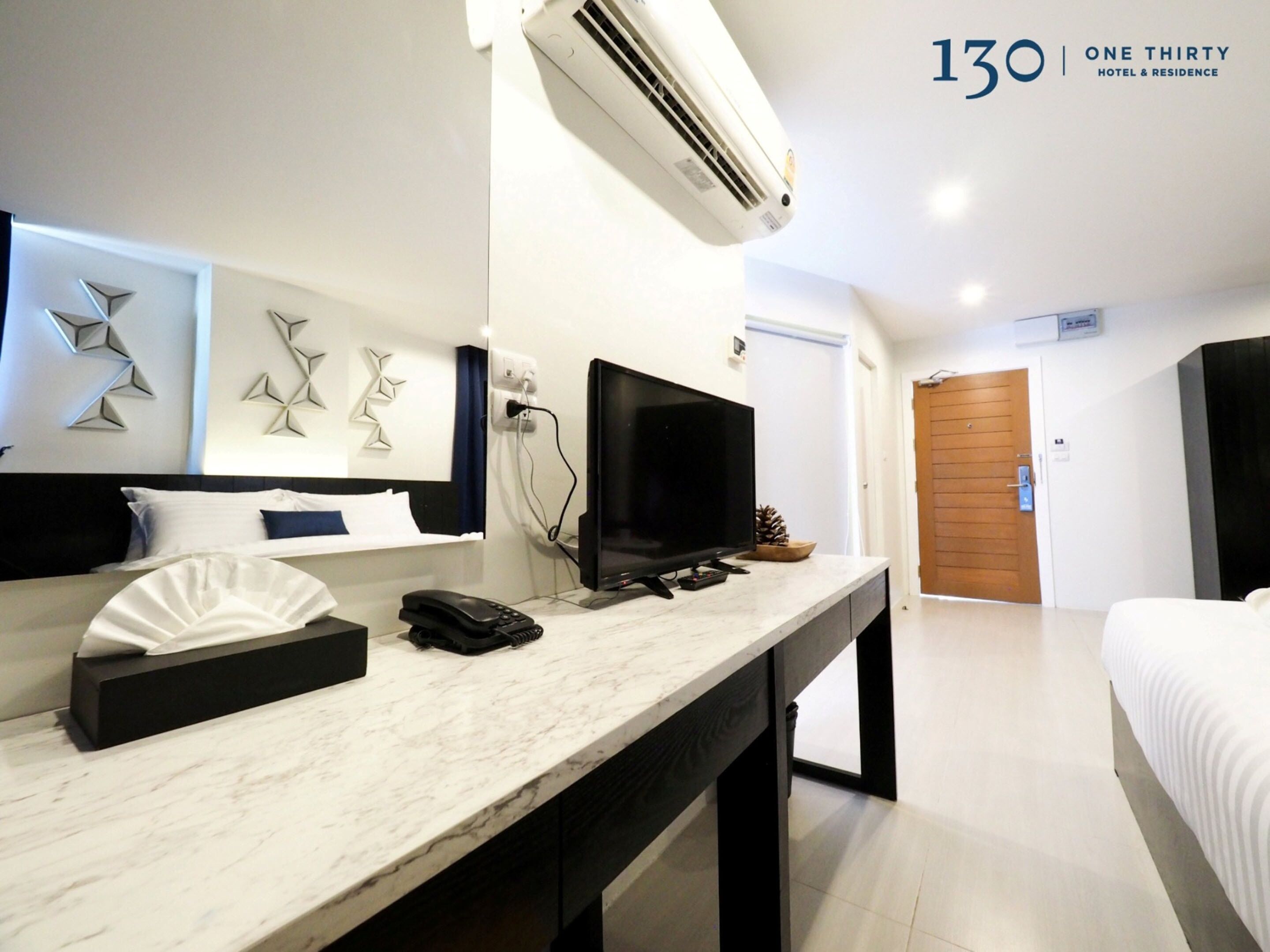 A modern hotel room with a marble desk, a flat-screen TV, a phone, and a bed with white bedding.