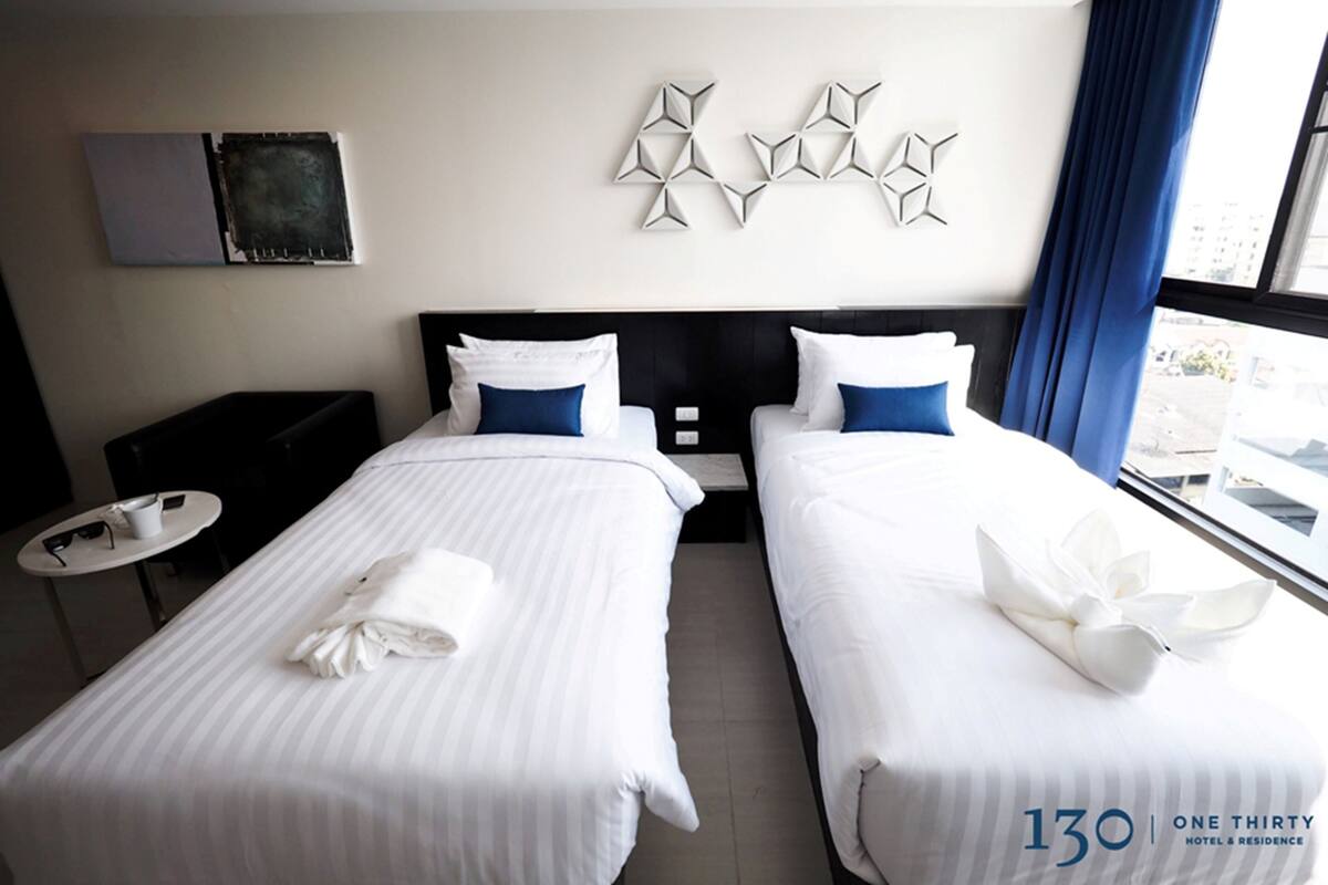 Une chambre d’hôtel avec deux lits, une petite table, un téléviseur et une fenêtre avec des rideaux.