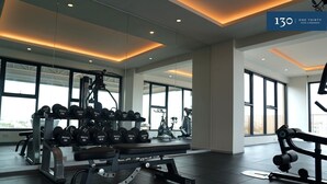 Une salle de sport moderne équipée de matériel de musculation, de machines de cardio et dotée de grandes fenêtres offrant une vue sur la ville.