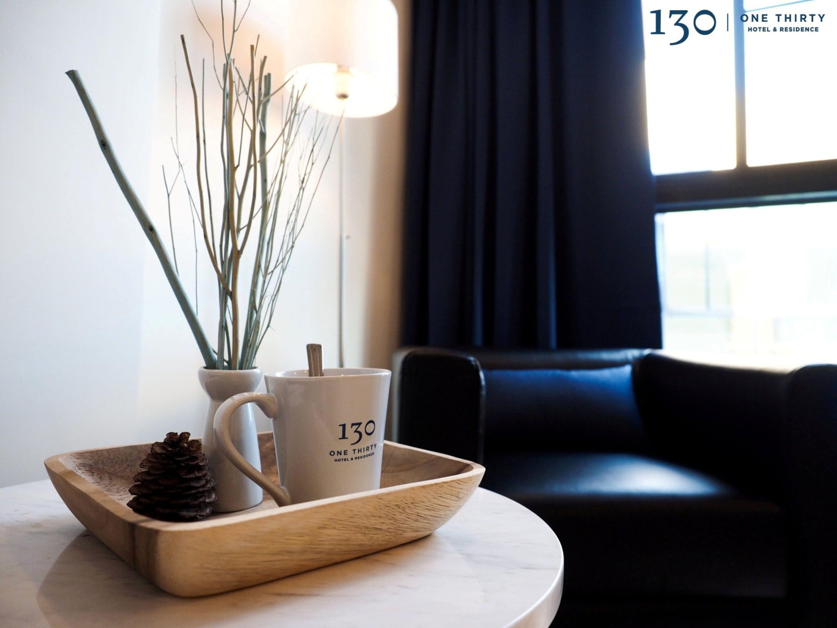 A wooden tray with a pine cone, a mug, and a vase with branches on a table.