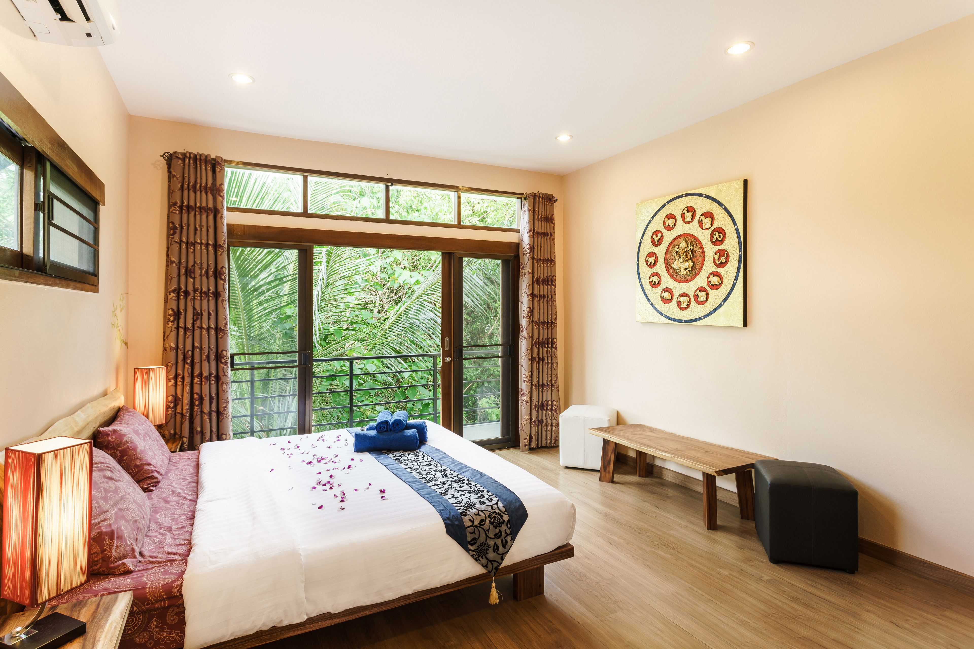 Une chambre à coucher avec un grand lit, un banc, une petite table et une œuvre d’art accrochée au mur.