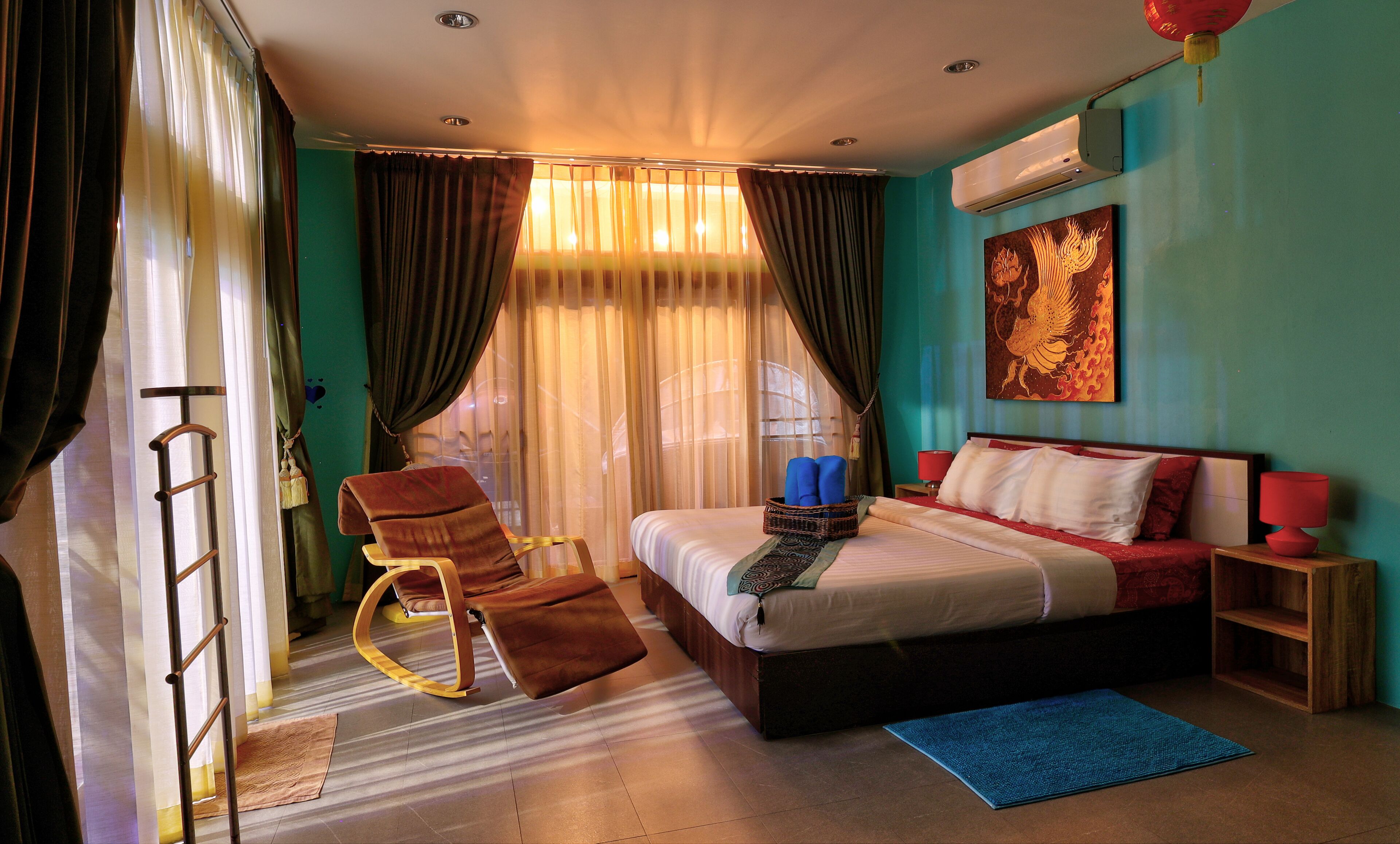 Een slaapkamer met een bed, een schommelstoel, een blauw vloerkleed en een wandairconditioning.
