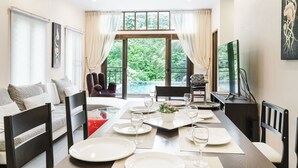 Un comedor con una mesa larga dispuesta para cuatro personas, un sofá y un televisor al fondo.