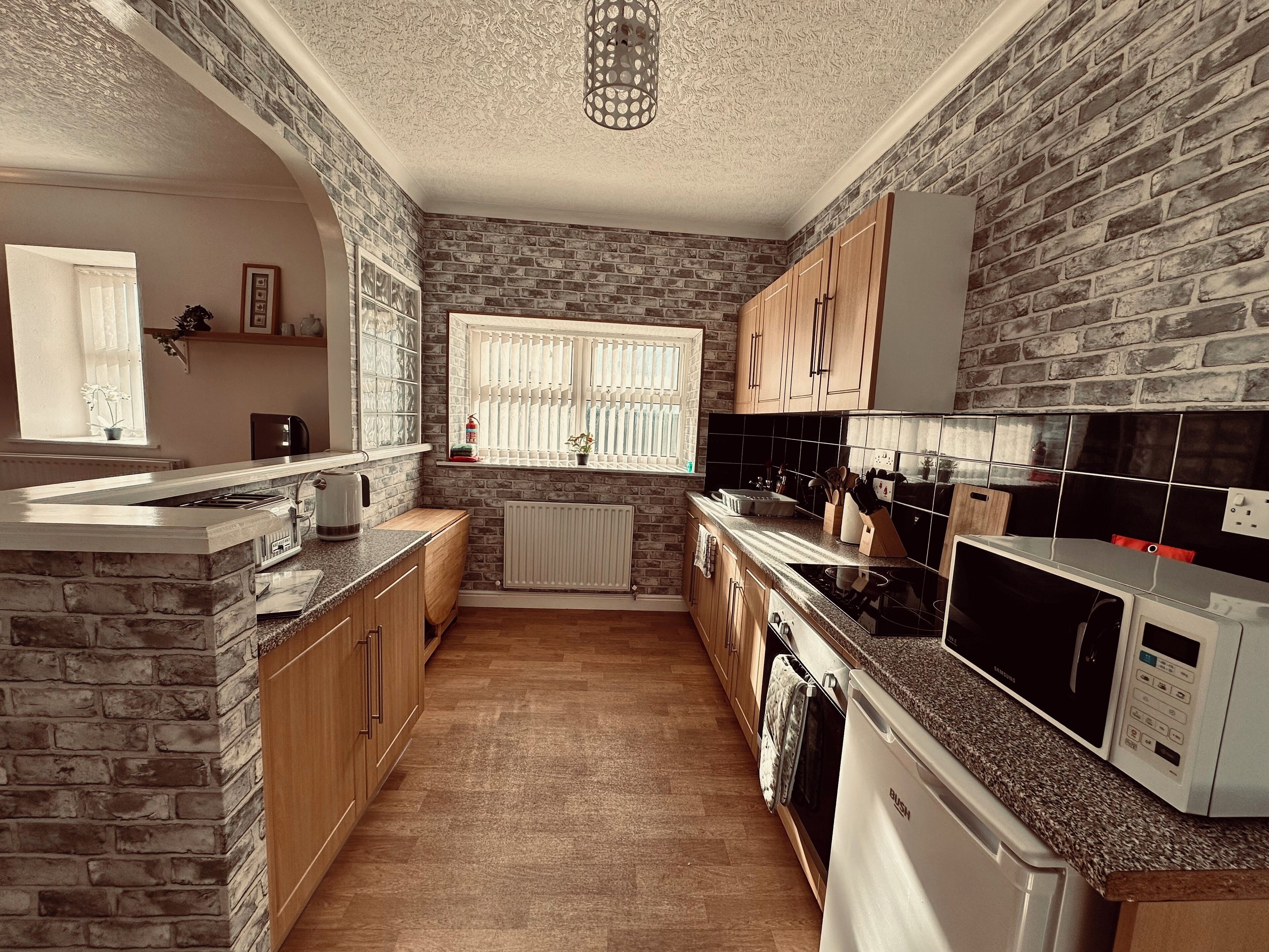 A kitchen with brick walls, wooden cabinets, a granite countertop, a built-in stove, a microwave, and a dishwasher.