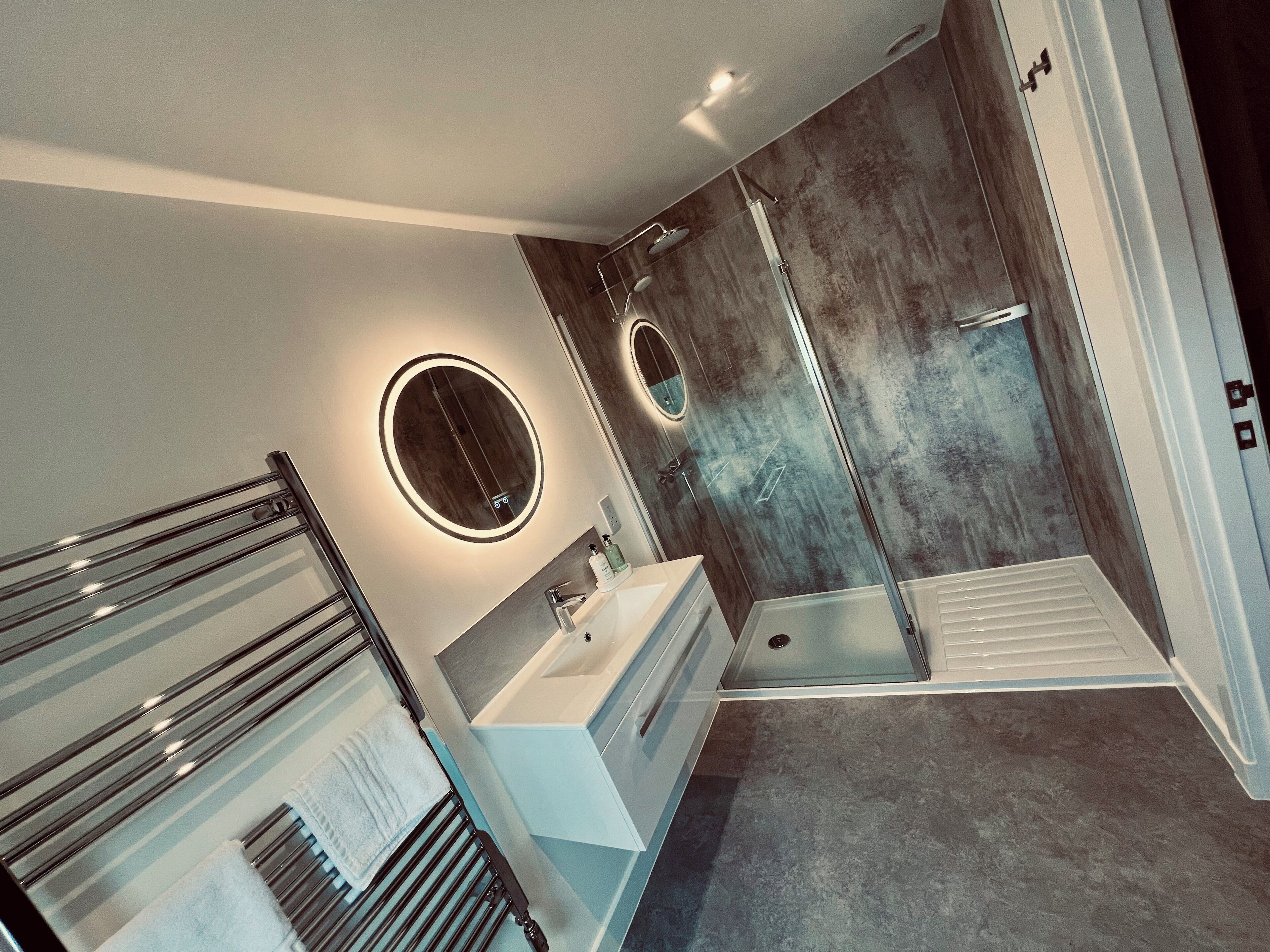 Un bagno moderno con cabina doccia in vetro, uno specchio rotondo e un mobile lavabo.