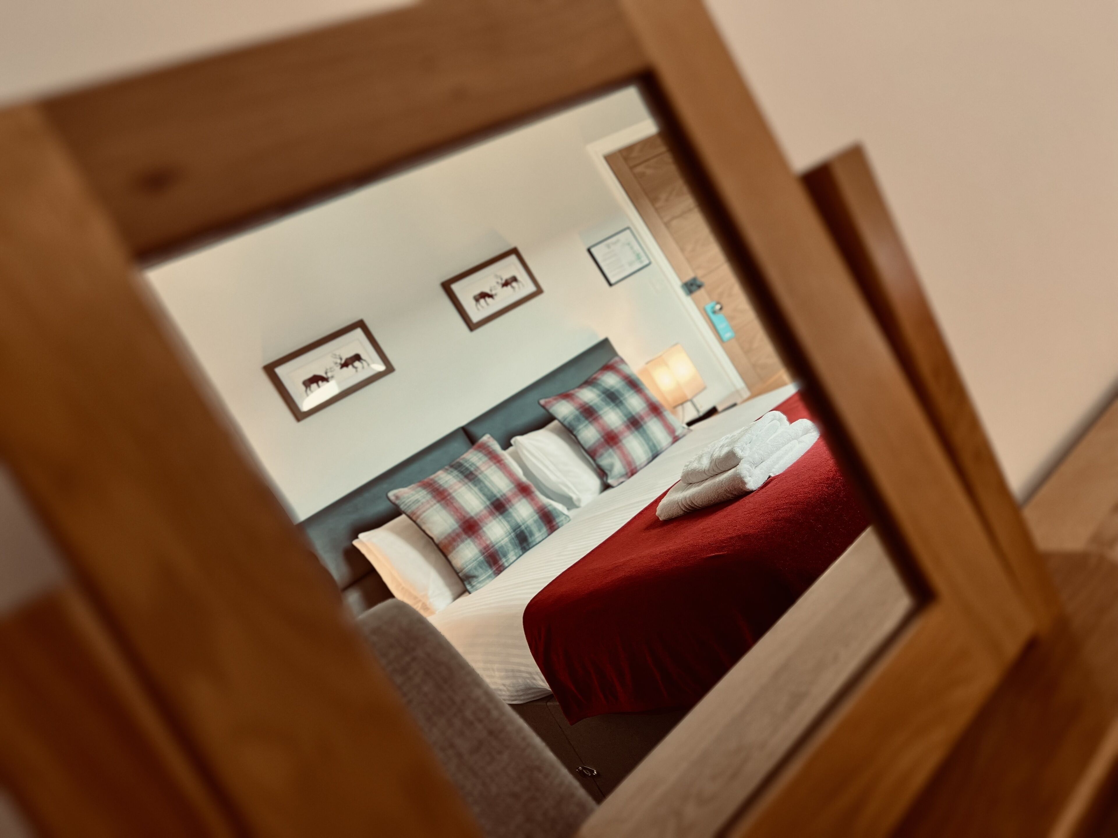 Un dormitorio con cama, almohadas, una colcha roja y cuadros en la pared.