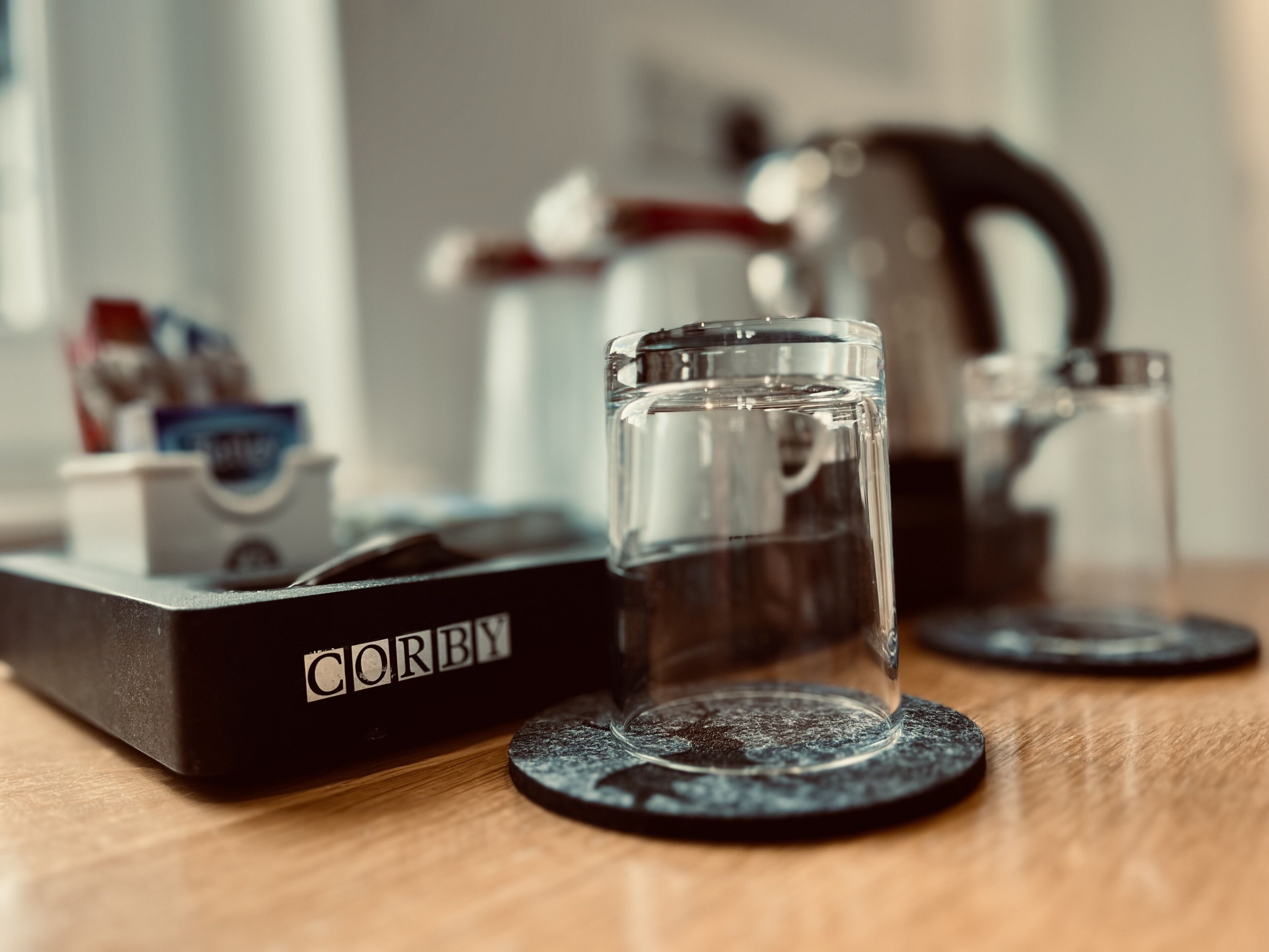 A coffee machine with a glass carafe and a box labeled "CORBY" on a wooden surface.