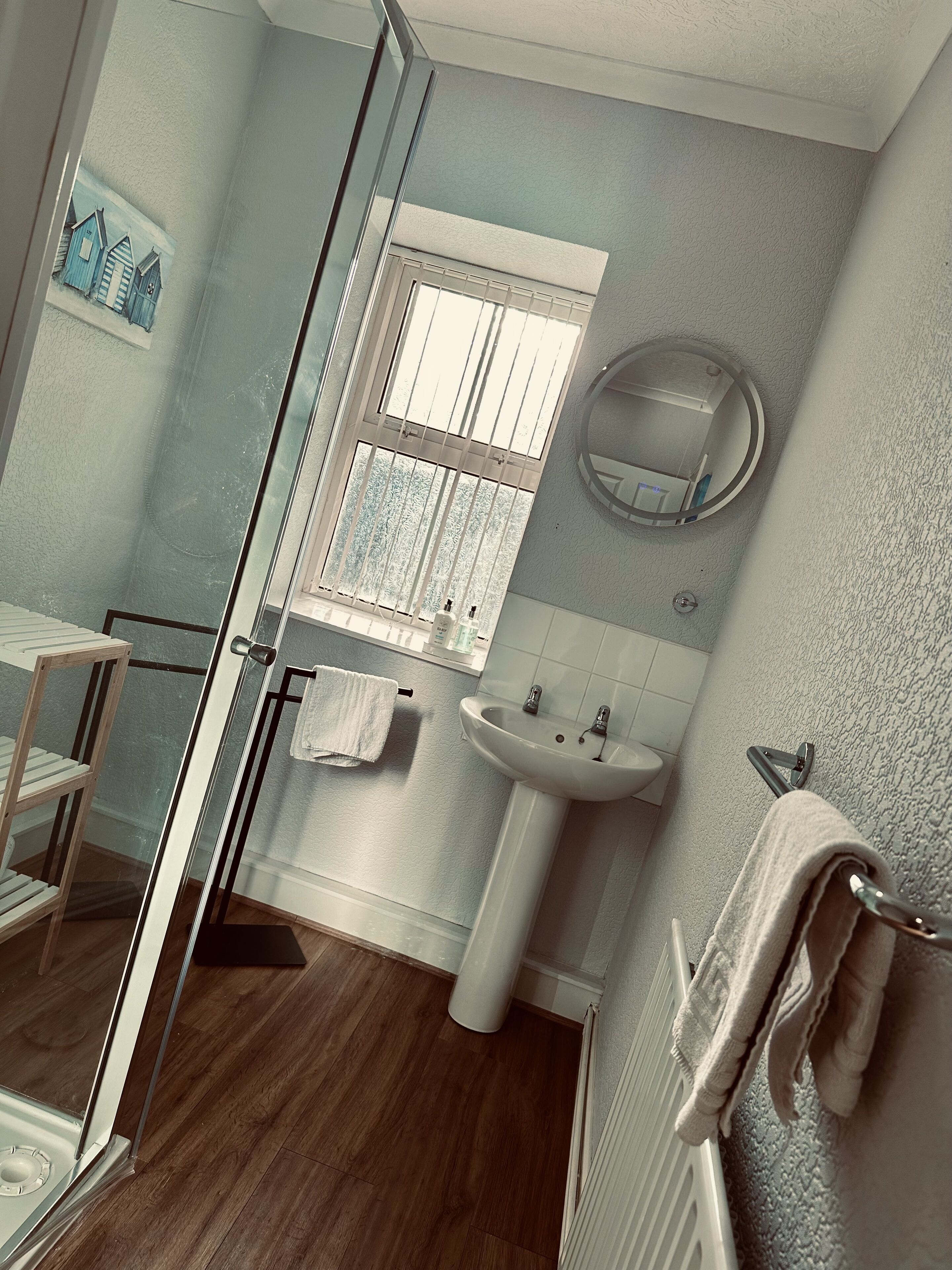 Une salle de bain avec une douche en verre, un lavabo, un miroir et une fenêtre avec des barreaux.
