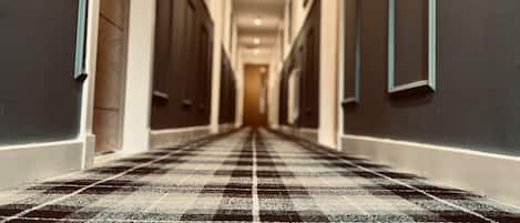 A hallway with a checkered carpet, doors on both sides, and a light at the end.