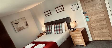 A bedroom with a bed, nightstands, a red blanket, a wooden wardrobe, and framed pictures on the wall.