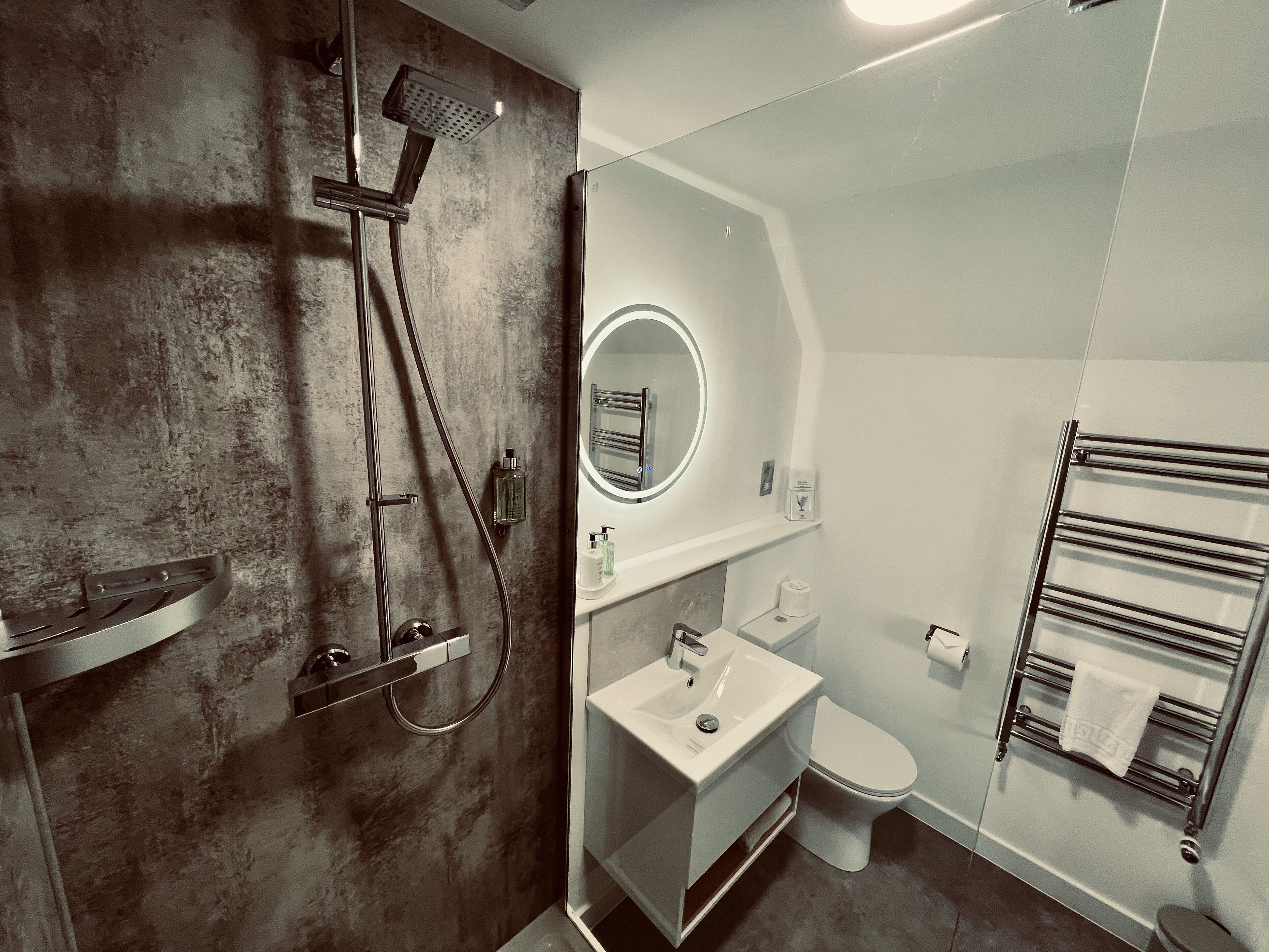 A modern bathroom with a shower, sink, toilet, and towel rack.