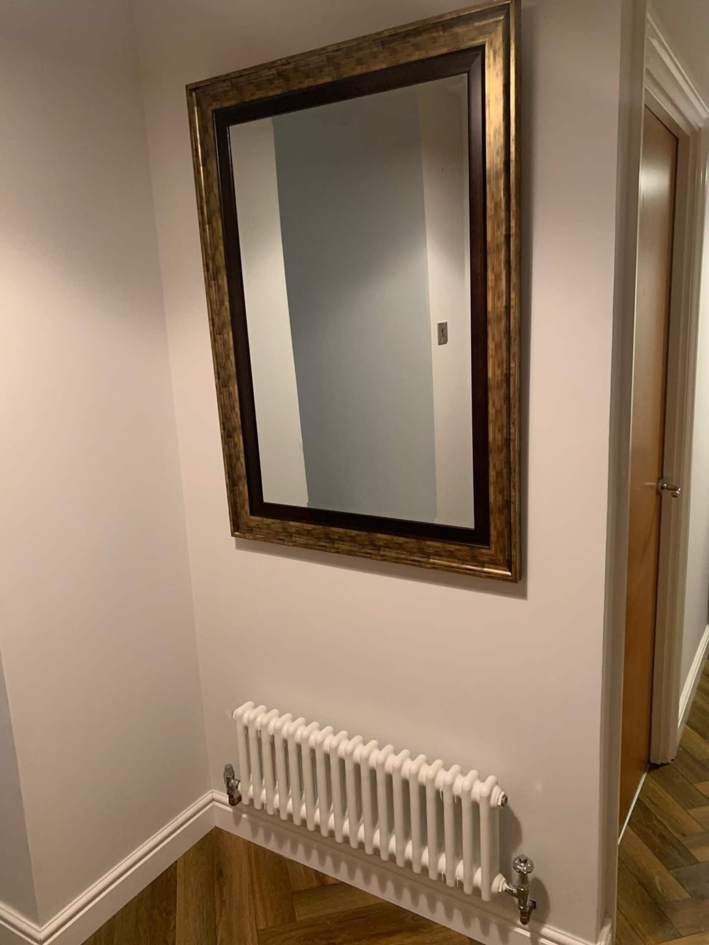 A hallway with a radiator, a framed mirror, and a wooden floor.