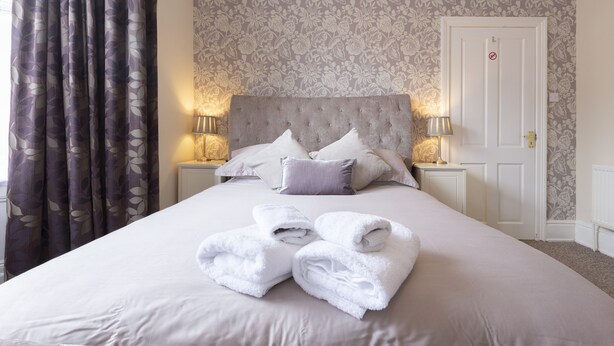 A neatly made bed with a tufted headboard, two bedside tables with lamps, and a door with a "no entry" sign. - Apartment 32 (York)