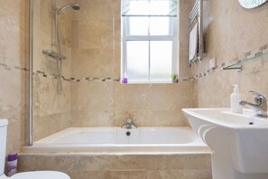 A bathroom with a bathtub, a shower, a sink, and a window. - Apartment 32 (York)