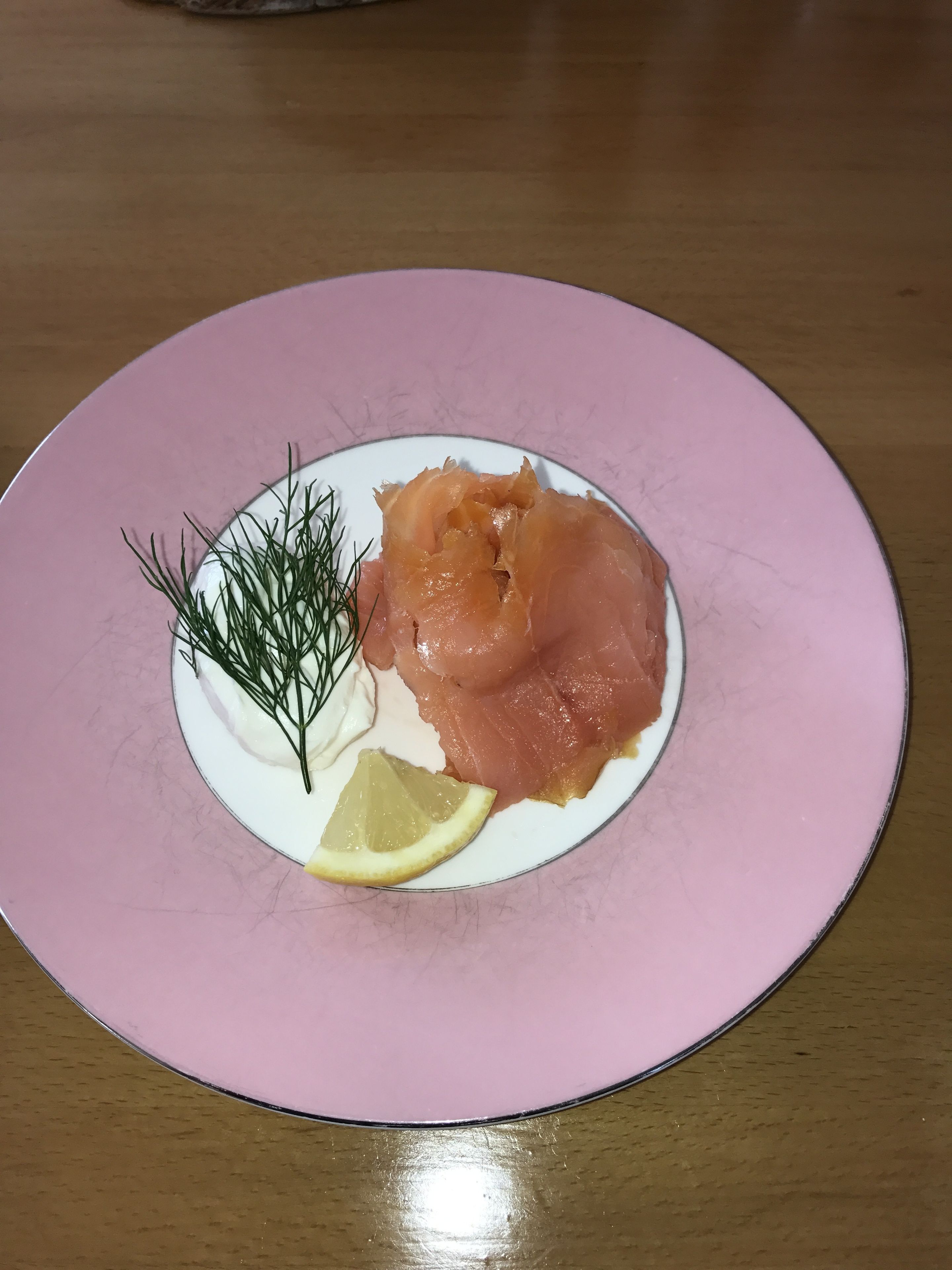 Lautasella on savulohta, tilliä ja sitruunaviipale, ja lautanen on vaaleanpunainen.