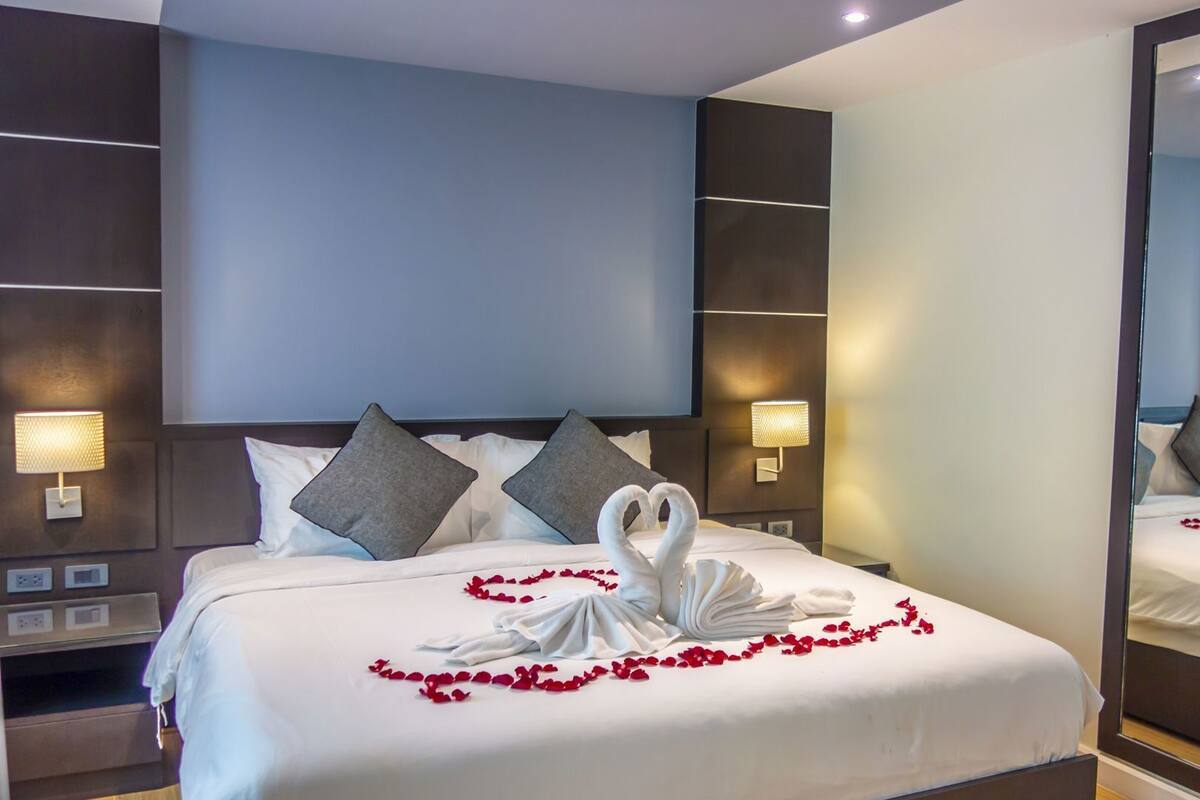 A hotel room with a large bed, two bedside lamps, a mirror, and a wall-mounted control panel.