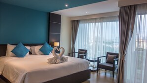Camera d'albergo con un letto grande, due poltrone, una scrivania e vista sulla città attraverso ampie finestre.