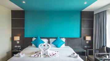 Ein Hotelzimmer mit einem großen Bett, zwei blauen Kissen, einem schwanenförmigen Handtuch und einem Glastisch.