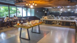 Un café moderne doté d’une longue table commune, d’un espace salon et d’une cuisine située à l’arrière-plan.