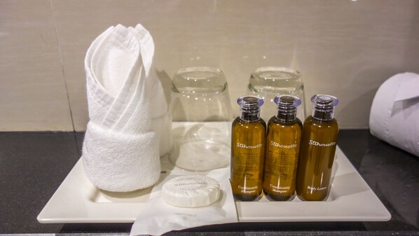 A bathroom vanity with a white towel, a round soap dish, and three bottles of body lotion and shampoo.