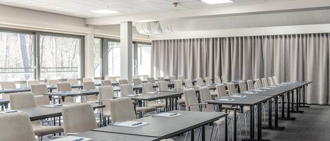 A conference room with multiple tables and chairs, large windows, and a projector on the ceiling.