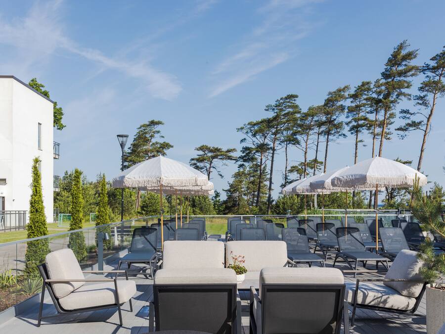 A rooftop lounge area with multiple lounge chairs and umbrellas, surrounded by trees and a building.