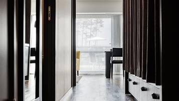 Um corredor com piso de madeira, uma cadeira preta e uma mesa com guarda-sol branco em frente a uma porta de vidro.