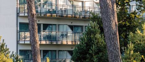 Un edificio moderno con varios balcones, rodeado de árboles y una hamaca.
