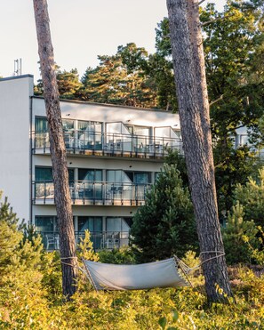 A modern building with multiple balconies, surrounded by trees and a hammock.