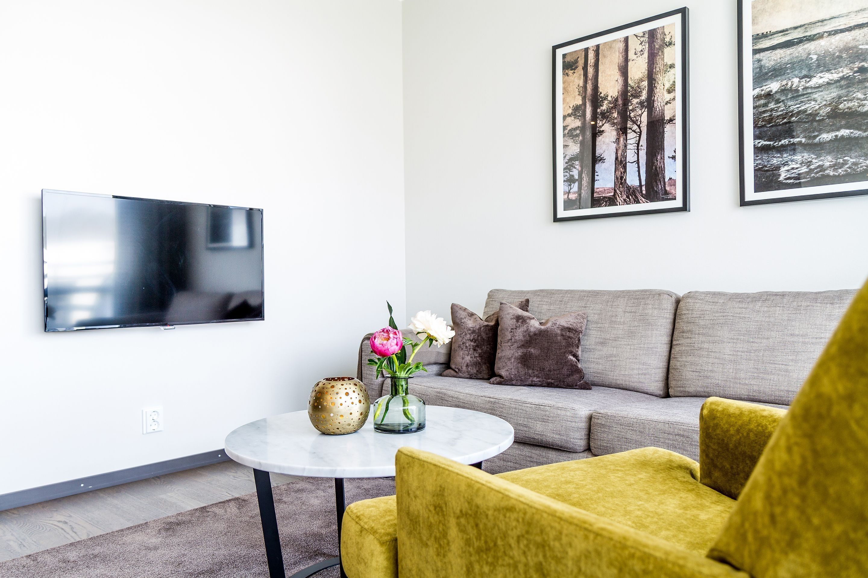 Ein modernes Wohnzimmer mit einem grauen Sofa, gelben Sesseln, einem runden Couchtisch und einem flachbildfernseher an der Wand.