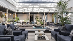 Un espacio interior amplio con muebles modernos, un área de estar central y un techo de cristal que permite la entrada de luz natural.