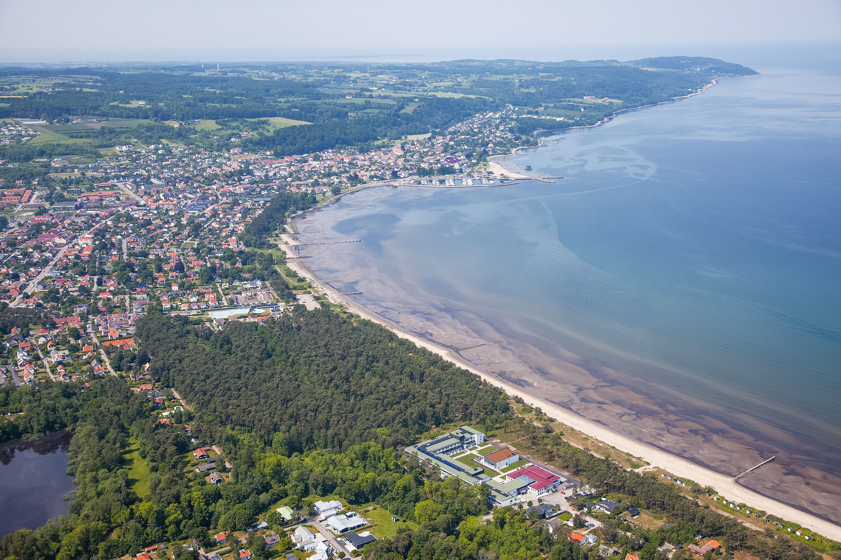 Ein Luftbild einer Küstenstadt mit Strand, dichtem Wald und Wohngebieten.