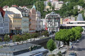 A riverside promenade with historic buildings, a bridge, and a tree-lined walkway. - Thalia (Karlovy Vary)