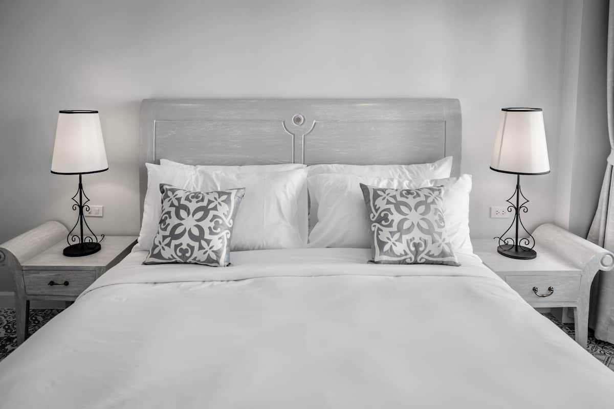 A neatly made bed with white bedding and patterned pillows, flanked by two bedside tables with lamps.