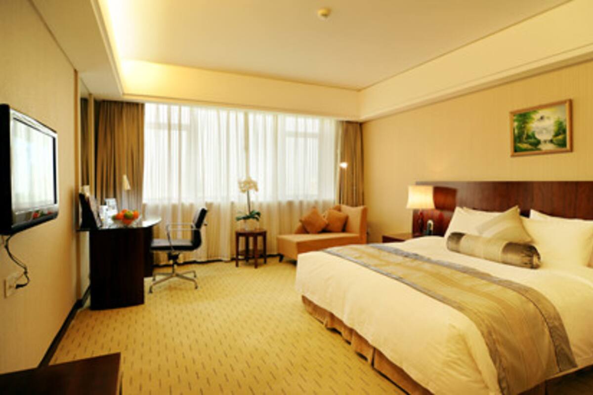 A hotel room with a bed, a desk, a chair, a lamp, and a painting on the wall.