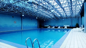 An indoor swimming pool with a blue color scheme, a metal roof structure, and lounge chairs along the poolside. - Sovereign Hotel KunShan (Suzhou)