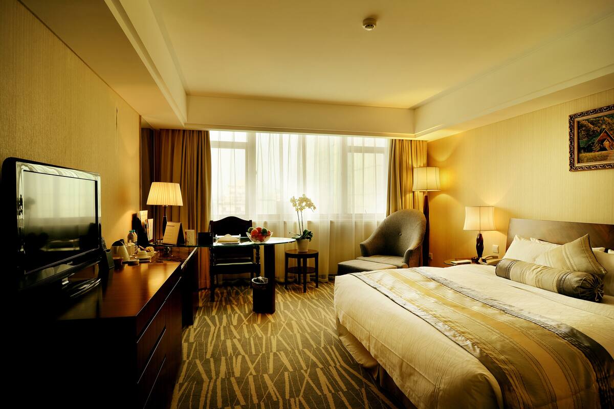 A hotel room with a bed, desk, chair, television, and a window with curtains.