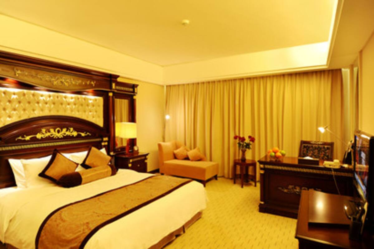 A hotel room with a large bed, a desk, a chair, and a desk lamp.