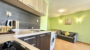 A modern kitchen with a built-in washing machine, wooden cabinets, and a grey sofa in a living area with green walls. - Menada Paradise Dreams Apartments (Sveti Vlas)