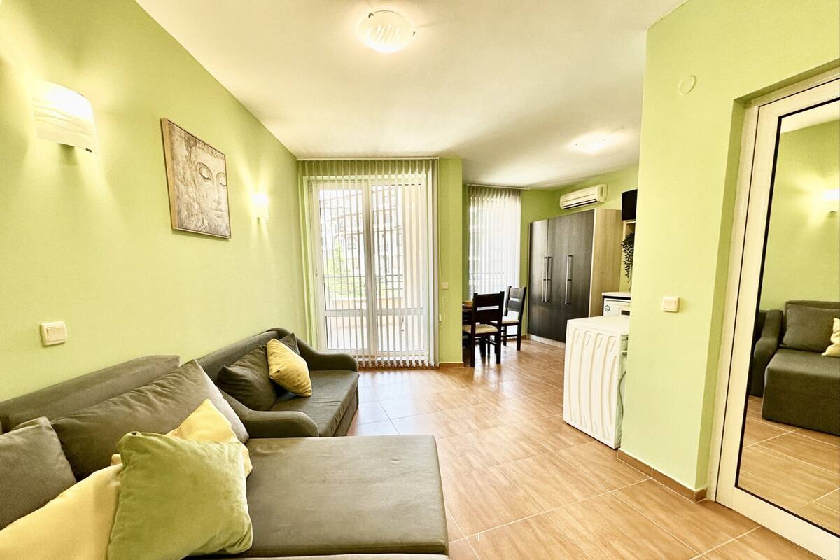 Ein Wohnzimmer mit Sofa, einem Esstisch mit Stühlen und einer Küchenzeile mit Kühlschrank.