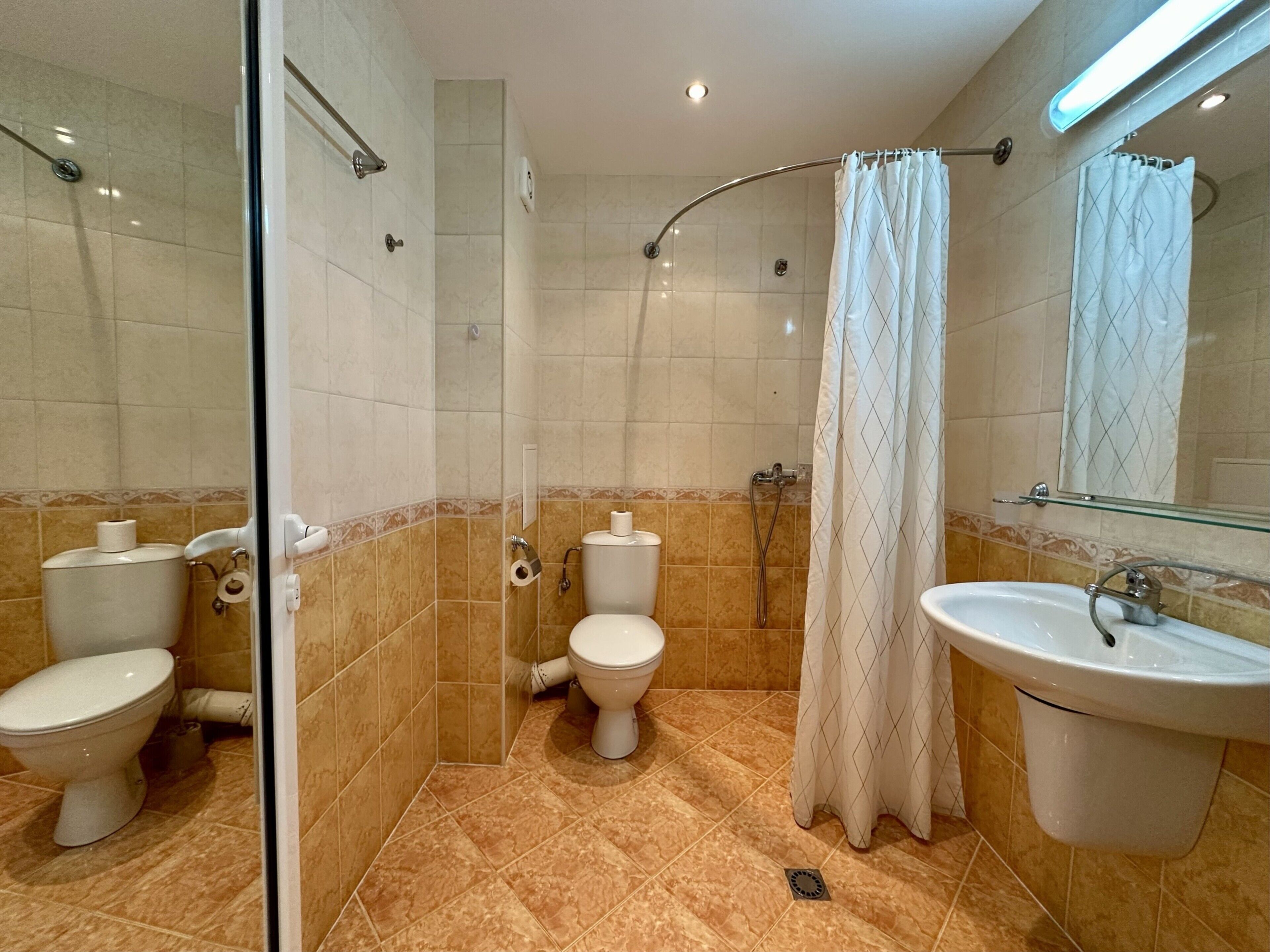 A bathroom with two toilets, a shower, and a sink.